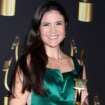 This picture is of Cristina Milizia - GVAA Co-Founder, Owner, & Coach. She's a latin women, with brown hair and brown eyes. She's pictured at the SOVAS awards, holding her winning trophy, wearing a shinny green dress.