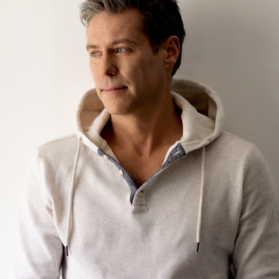 A photograph of a trim white man with short cut hair wearing a fitted sweatshirt, gazing off to the left with a small smile.